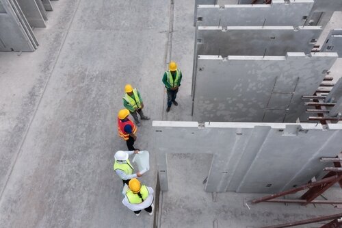 Aerial top view of architect and engineer discussing building plan at construction building site in warehouse factory. Precast concrete manufacturing products on prefabricated house factory